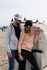 A grey hoodie and a black cap on a model beside a woman in a pink sweater and black cap, at a beach setting.