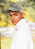 A man wearing a grey cap and a white hoodie, with a blurred outdoor background. The cap features a logo.