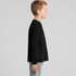 A black long-sleeve t-shirt displayed on a model facing sideways, paired with grey pants. It features a logo.