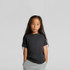 A child wearing a black heavy faded tee, with long hair and hands in pockets, set against a neutral background.