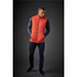 An orange thermal vest worn by a man, featuring a quilted design and a branding logo.