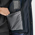 A hand reaching into a grey inner pocket of a navy blue jacket featuring a logo.