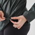 A dark green women's wind jacket with a drawstring at the hem being adjusted by hands.
