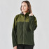 A woman models a green and dark green Women's Vertex Stormshell jacket with a hood. The jacket features a logo.