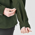 A woman’s green jacket with a logo, featuring an adjustable cuff and a zippered pocket.