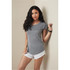 A woman in a grey T-shirt with short sleeves poses against a wall, wearing white shorts. The shirt has a logo.