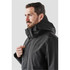 A man wearing a black Magellan System jacket, featuring a hood and front zipper, with a logo visible.