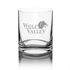 A clear glass whisky tumbler featuring a logo and a sturdy base. The glass has a polished finish.