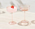 A set of two pink coupe glasses, one filled with a drink and garnished with a strawberry, displayed on a light surface.