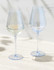 A set of two elegant blue-tinted wine glasses, one filled with white wine, presented on a light surface.
