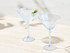 A set of two elegant clear martini glasses with a light blue tint, featuring one with an olive garnish.