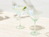 A set of two clear glass glamour martini glasses with green accents, featuring a cocktail garnished with an olive.