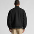 A black felt bomber jacket viewed from the back, featuring a ribbed collar and cuffs. It has a logo.