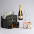 A drink bottle with a grey blanket, two glasses, a bottle of sparkling wine, and assorted snacks in packaging.