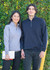 A grey and a navy half zip fleece jumper are worn by a woman and a man, standing together outdoors with greenery in the background.