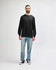A long sleeve t-shirt in dark grey worn by a model, paired with black trousers and sneakers.