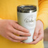 A drink bottle in light grey with a clear lid, featuring a logo, held by hands in front of a yellow sweater.
