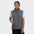 A women's puffer vest in grey, featuring a zip front and side pockets, worn over a white top.