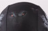 A black swimming cap featuring a graphic design with fierce eyes and a textured pattern. It has a logo.