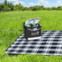 A black cooler bag sits on a checkered picnic blanket in a grassy field, with drinks visible inside.