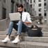 A black laptop briefcase sits on steps beside a man working on a silver laptop, dressed in a white shirt and tie.