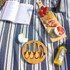 A wooden serving board with assorted snacks, including strawberries, crackers, and dips, on a striped blanket.