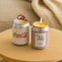 A collection of six candle boxes in various pastel colours, with a silver can candle among them. Each box has a logo.
