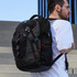 A black backpack with red accents is worn on the back of a person standing on steps, featuring multiple compartments and a logo.