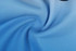 A fabric swirl showcasing light blue material, featuring a smooth texture. The image includes a logo in a corner.
