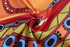 A vibrant beach towel featuring a bold pattern with orange, red, yellow, and blue colours. It has a logo.