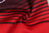 Red and dark brown striped fabric, featuring a smooth texture, with a logo visible on the material.