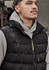 A unisex black hooded puffer vest is worn over a grey hoodie. The vest features a logo and a zip closure.