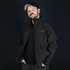 A man wearing a black Swiss Peak Urban Softshell Jacket with a logo, against a dark background.