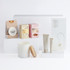 A white candle with a wooden lid, caramel fudge, drink chocolate, marshmallow treats, and skincare tubes in neutral tones.