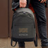 A grey backpack with a logo, being held by a person wearing dark clothing.