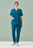 A woman stands wearing teal scrub top and bottom with pockets, paired with casual shoes, against a soft background.