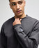 A grey adult crewneck sweatshirt with a branded logo on the sleeve, featuring a relaxed fit and soft fabric.