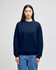 A navy blue crewneck sweatshirt is worn by a model, featuring a small logo on the sleeve.