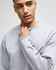 A grey crewneck sweatshirt on a model, featuring a logo on the sleeve. The fabric appears soft and comfortable.
