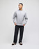 A grey crewneck sweatshirt with long sleeves, paired with dark trousers and casual shoes. The model stands against a plain background.
