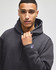 A dark grey pullover hooded sweatshirt on a model, featuring a logo on the sleeve.