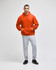 An orange pullover hooded sweatshirt is worn with grey track pants, complemented by black shoes.