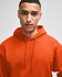 An orange pullover hooded sweatshirt is worn by a model, featuring a drawstring hood.