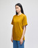A mustard yellow short-sleeve t-shirt on a model, featuring a logo on the sleeve.
