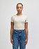 A beige women's crop fitted T-shirt displayed on a model, paired with blue jeans. Features a logo.