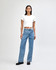 A woman stands wearing a white crop fitted T-shirt and blue jeans, with black shoes, against a light background.