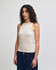 A fitted tank top in a light beige colour, featuring a high neckline and worn with dark jeans. The model has curly hair.