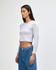 A light grey, long-sleeved, cropped fitted t-shirt on a model, paired with blue jeans. It features a logo.