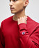 A long-sleeve t-shirt in red, featuring a small logo on the sleeve, worn by a model.