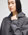 A grey cropped hoodie with a hood, featuring a logo on the sleeve.